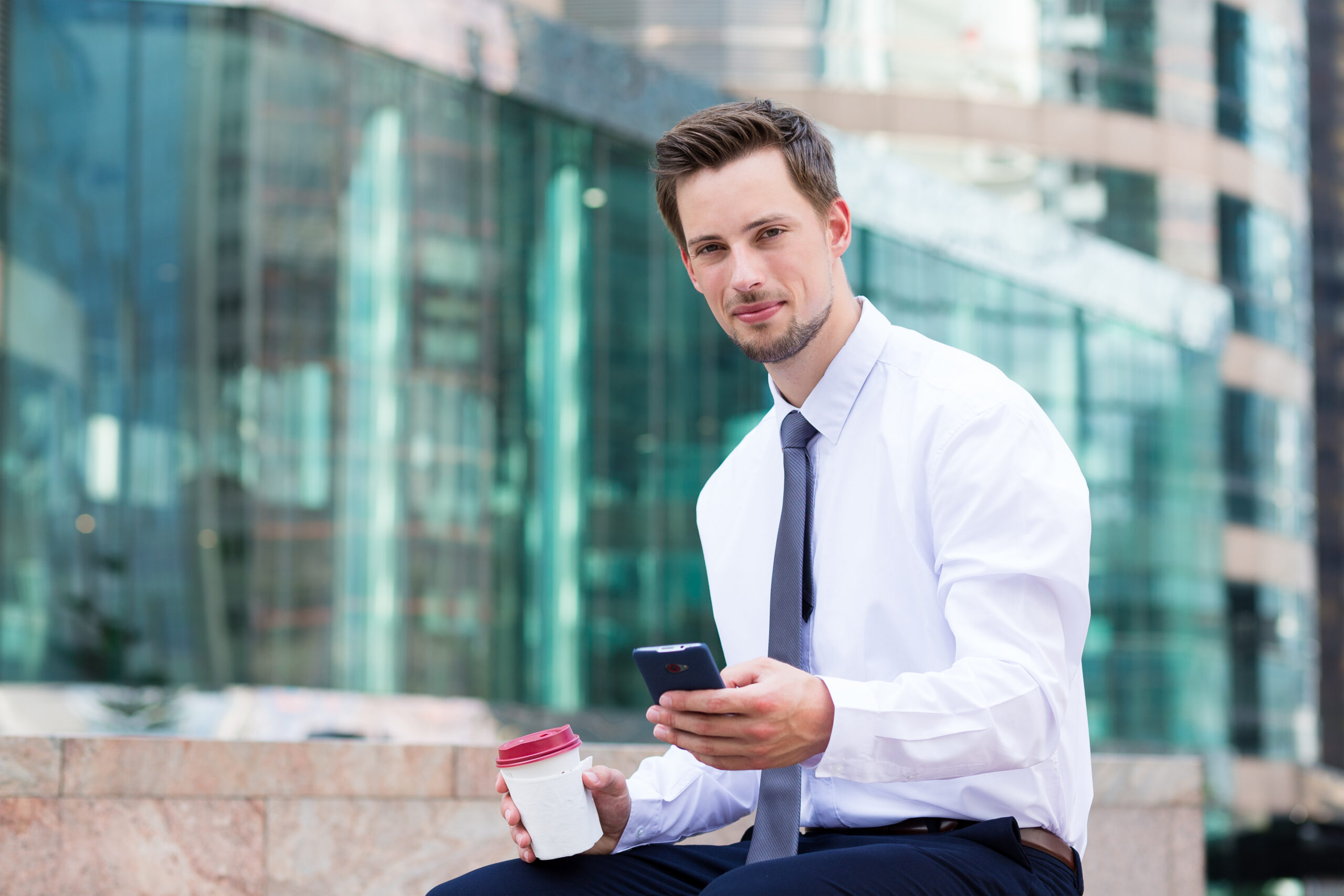 young-businessman-sitting-with-coffee-and-smartpho-2023-11-27-05-35-07-utc-scaled.jpg